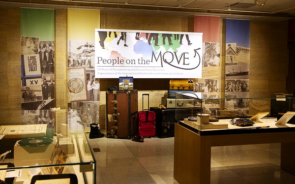 An image of the "People on the Move" exhibit showing the title banner, display cases and suitcases.