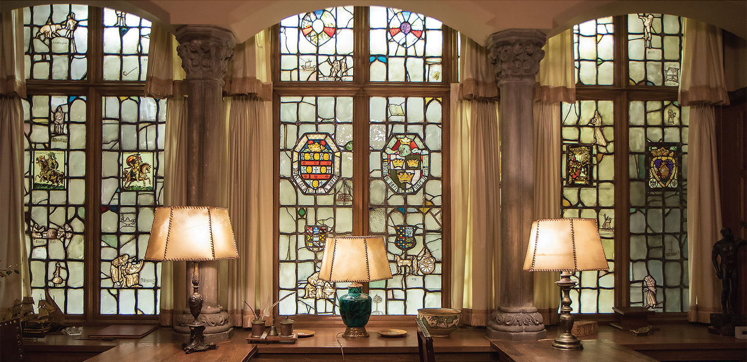 One side of the Bell Period Room with three stained glass windows and three lit lamps