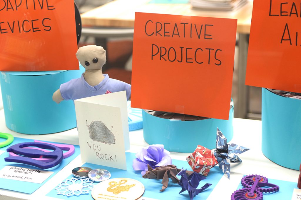 a display table showing sample projects created in the Makerspace, including 3D printed items, oragami creatures, and lasercut items