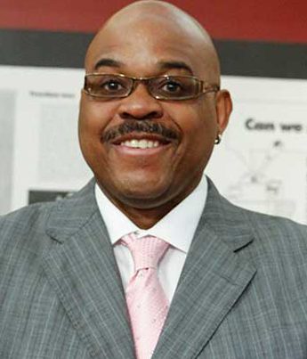 Headshot of smiling man wearing a gray blazer with a pink tie