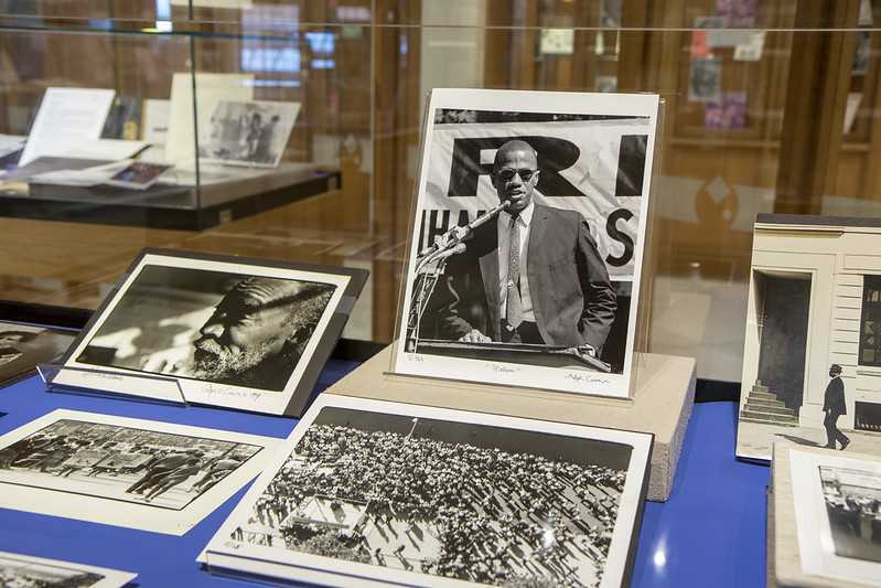 Exhibit case with a selection of photos by Adger Cowans, including a central photo of Malcolm X