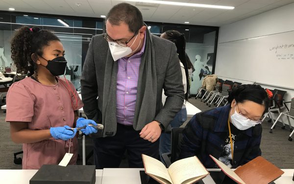Two students and a faculty member looking at rare books.
