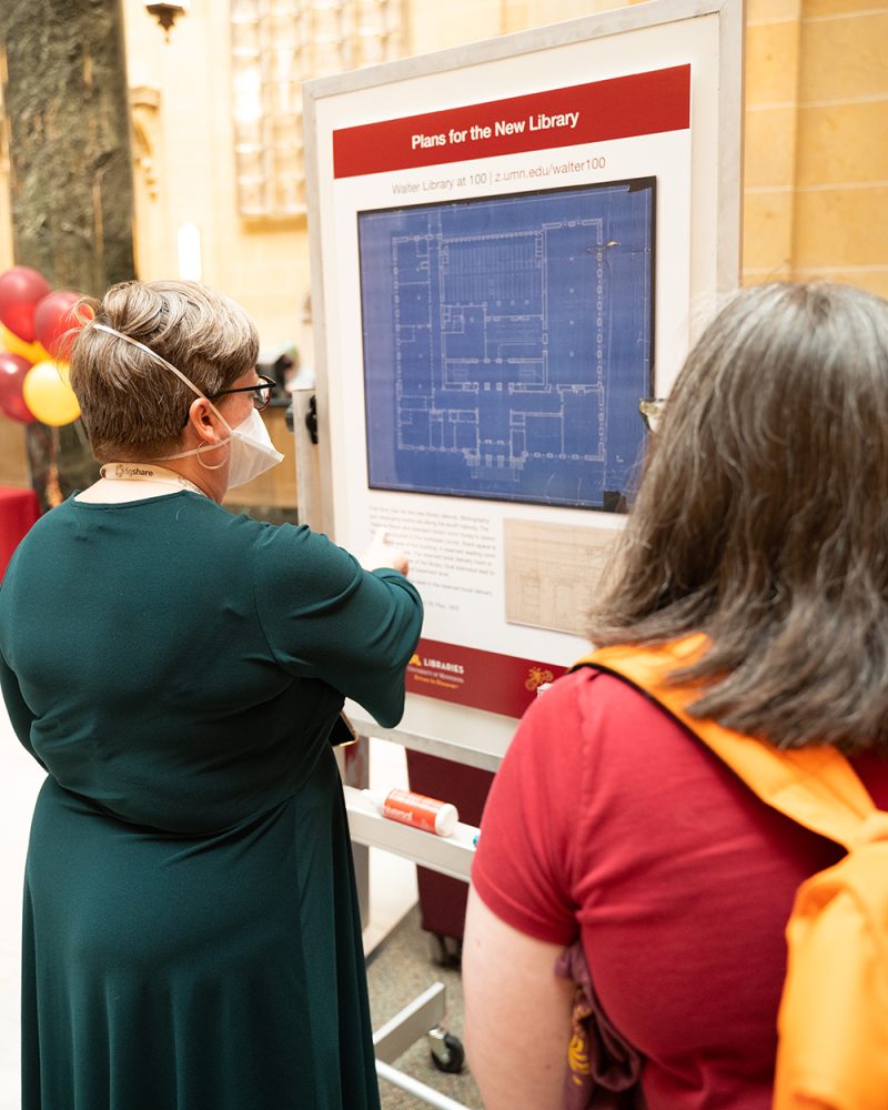 Two staff members read a poster that reads, "Plans for the New Library"