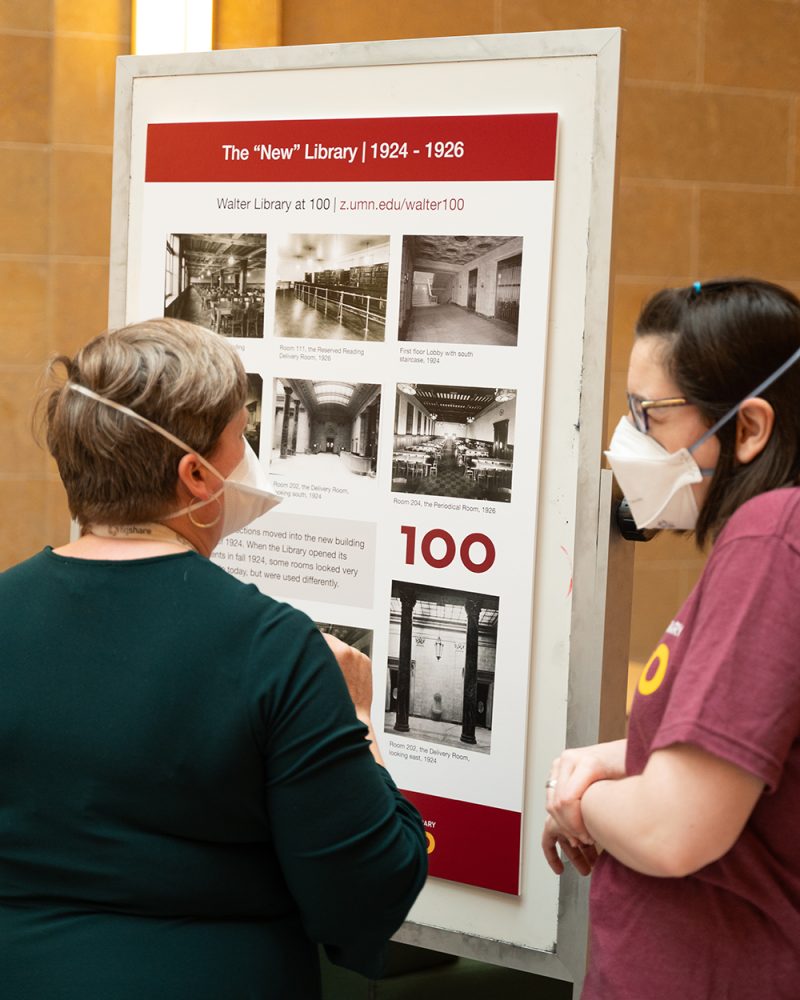 Two staff members read a poster that reads, "The New Library"