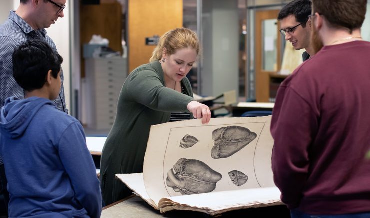 Students looking at oversized rare book.