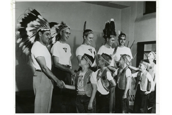 Men and boys wearing Indian headbands and feathers shaking hands, created between 1940 and 1969.