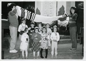 Archival image of eight children standing in two rows on a dais with two adults holding a blanket above them at the Temple Israel Duluth building from the Upper Midwest Jewish Archives