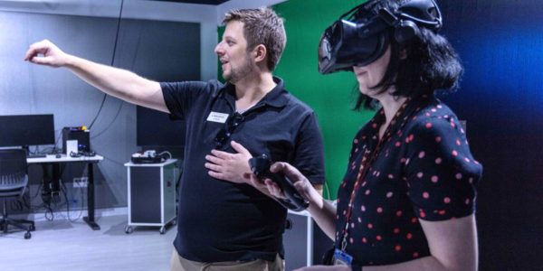 Two people, one pointing and the other wearing a virtual reality Headset.