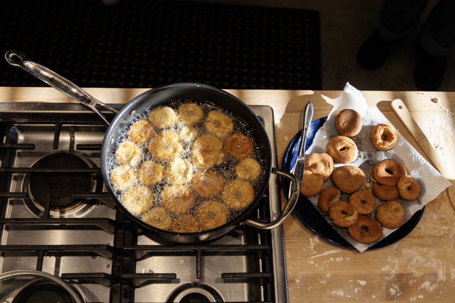 A saucepan full of beignets frying in hot oil, pictured next to a plate full of cooked beignets that have just finished frying
