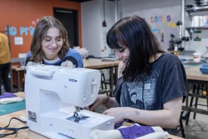 Two students using a sewing machine.
