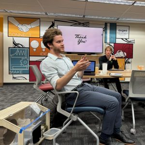 Evan Gils (male) sits at a table talking with others.