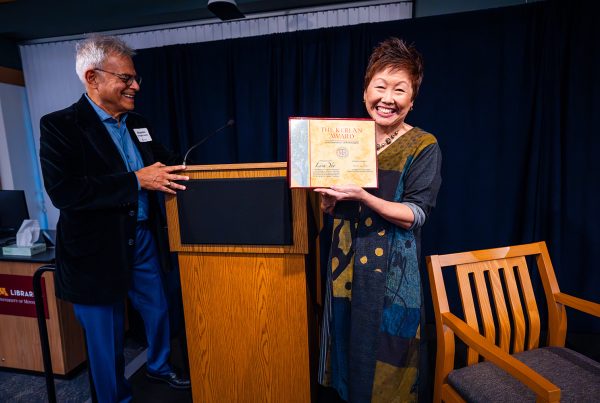 Man stands next to a podium while next to him a smiling woman holds up a certificate that says "The Kerlan Award"