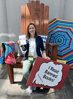 Melissa Ernst sitting in a large holding a sign that says, "I read banned books."