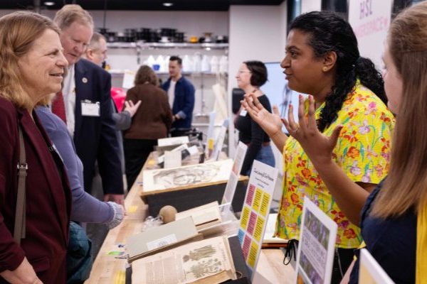 Four individuals looking at and talking with each other, with a table of rare books open between them.