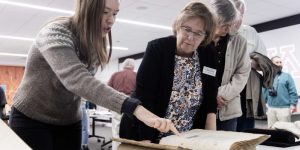 Several people in conversation as they explore a large rare book together.