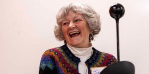 Woman with short gray hair standing at the podium and smiling.