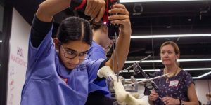 High school girl in scrubs practices drilling into a bone.