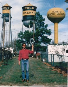 Larry Long stands by the water towers in Okemah, Oklahoma, the hometown of Woody Guthrie. Image courtesy of Long.