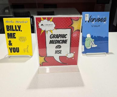 Two graphic novels on display in the Health Sciences Library, with a sign for the book display.