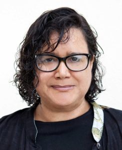 Headshot of Dr. Monica Green wearing glasses with curly hair against a solid background