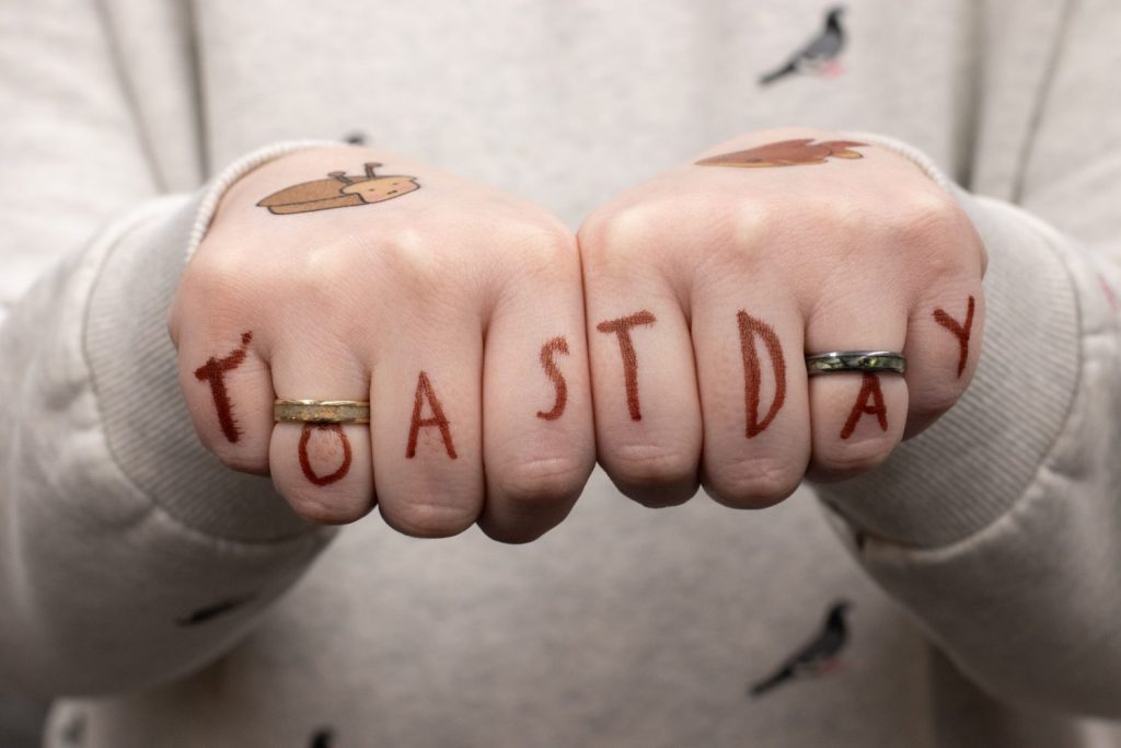 A person place their hands together in fist and the fingers have writing that spell out Toast Day.