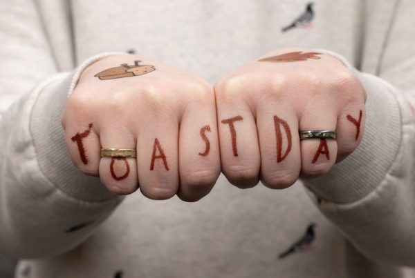 A person place their hands together in fist and the fingers have writing that spell out Toast Day.