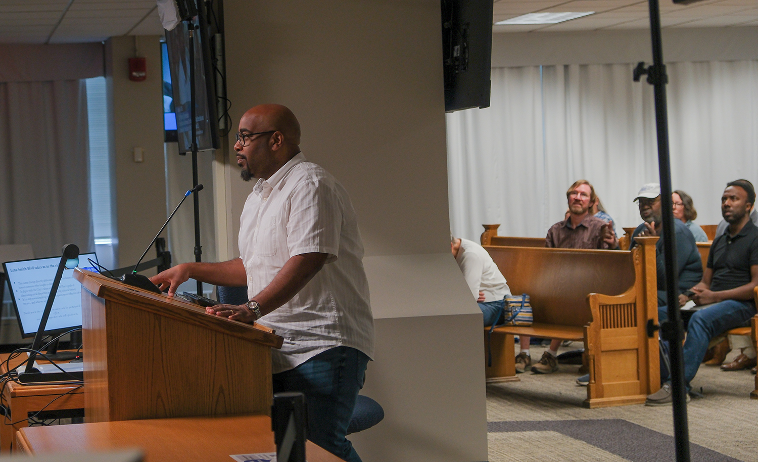 Man speaks into a microphone at a podium in front of an audience at a Minneapolis Planning Commission meeting
