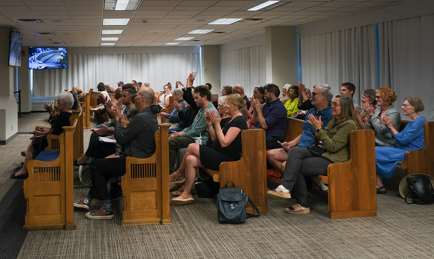 Room full of people sitting in wooden benches and clapping
