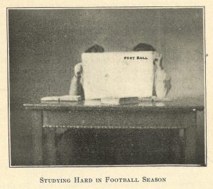 Image printed in an issue of the Ariel student newspaper depicting two students seated at a desk holding an issue of the publication FOOT BALL in front of their faces. The image includes the caption, "Studying Hard in Football Season."