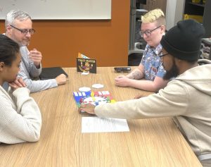 Four individuals sitting at a table playing a board game.