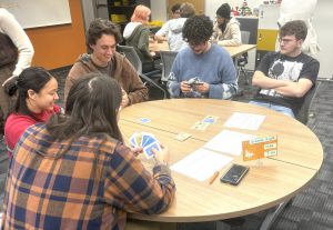 Students are sitting at a table playing a card game.