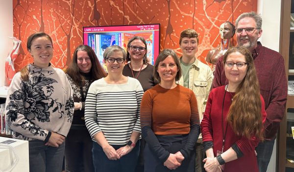 Eight members of the Health Sciences Library staff are shown at the library's service desk.